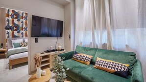 Een moderne woonkamer met een groene bank, een flatscreen televisie aan de wand en een groot raam met dunne gordijnen.
