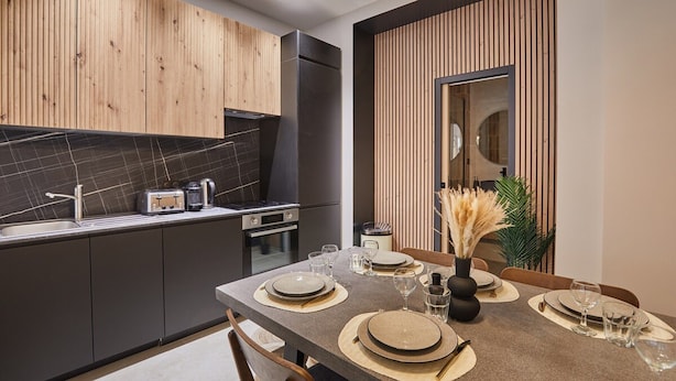 Een moderne keuken met donkere kastjes, een marmeren spatwand, en een eethoek voor vier personen met een centraal kookeiland.
