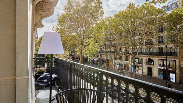A balcony with a white table and chairs, overlooking a street with trees and buildings. - Superb New 1 Bedroom Flat Notre Dame de Paris (Paris)