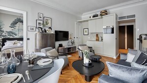 A modern hotel room with a dining area, a living room with a sofa and coffee table, a TV, and a kitchenette. - Superb New 1 Bedroom Flat Notre Dame de Paris (Paris)