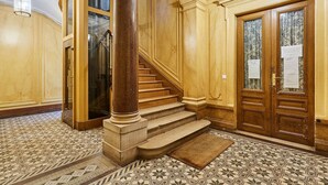Una imponente escalera con escalones de mármol que conducen a un segundo piso, flanqueada por puertas de madera con paneles de vidrio y un piso con diseño.