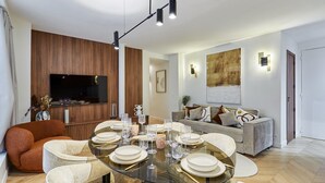 Una sala de estar moderna con una mesa de comedor de vidrio preparada para seis comensales, un sofá, un televisor y una pared de acento de madera.