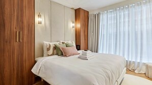 Un dormitorio con una cama grande, un armario de madera y una ventana con cortinas traslúcidas.