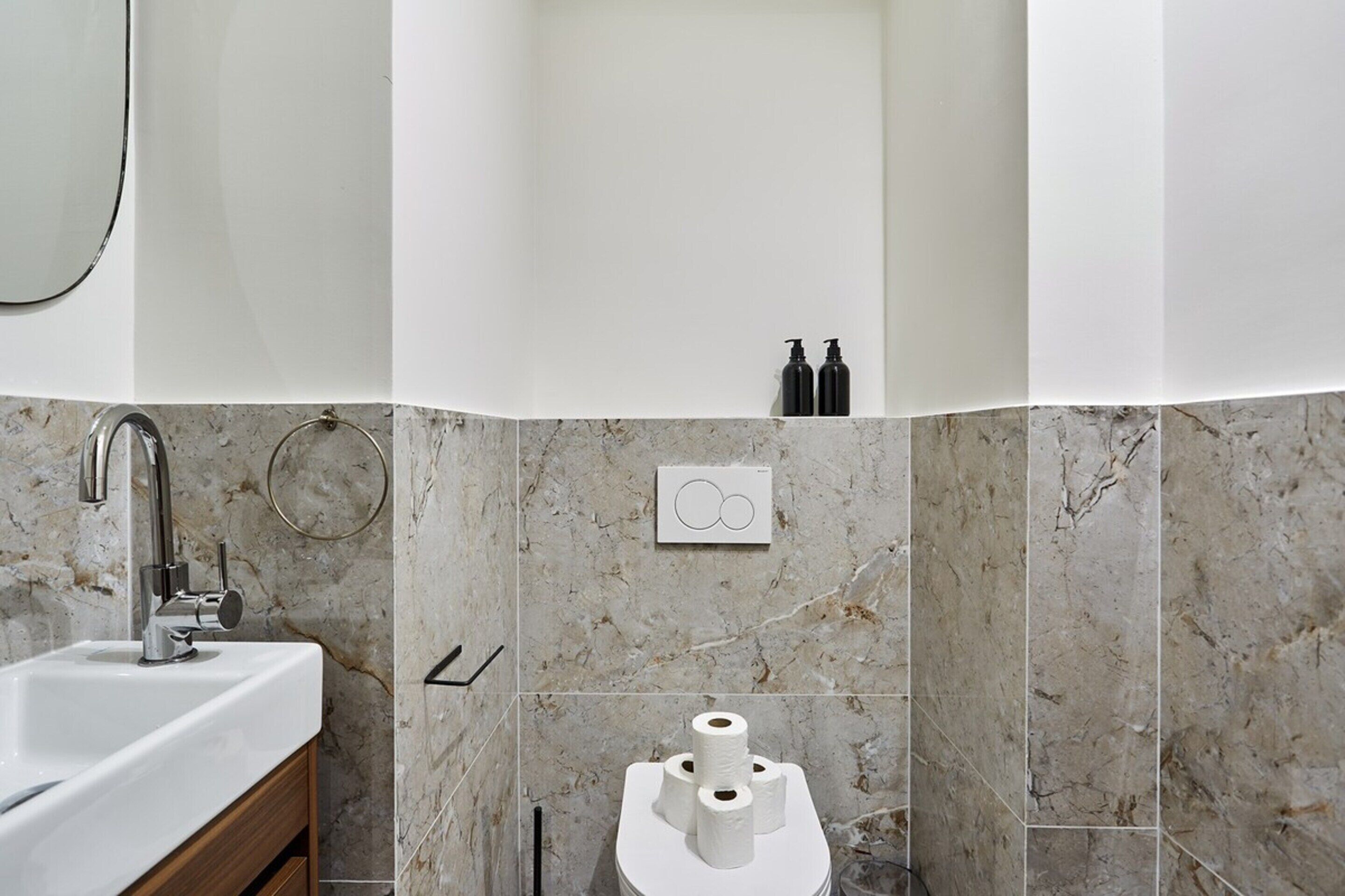 Ein Badezimmer mit Marmorwand, einem Waschbecken, einer Toilette und zwei Kosmetikartikeln.