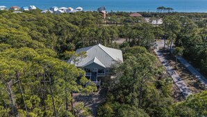 A large house surrounded by dense pine trees, with a view of the ocean and other houses in the background. - Back on the Rental Market! Dog-Friendly, 4BR/4BA w/ Pool! (St. George Island)