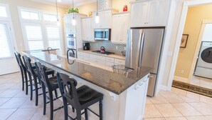 A modern kitchen with a large island, stainless steel appliances, and a seating area with chairs. - Back on the Rental Market! Dog-Friendly, 4BR/4BA w/ Pool! (St. George Island)