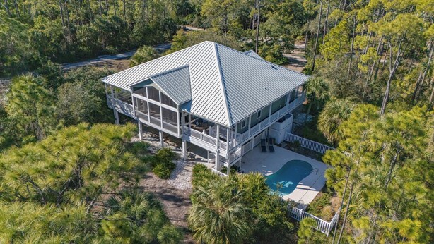 A large, two-story house with a metal roof, surrounded by dense pine trees. - Back on the Rental Market! Dog-Friendly, 4BR/4BA w/ Pool! (St. George Island)