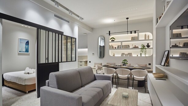 A modern living room with a grey sofa, a wooden coffee table, and a dining area with chairs and a table.