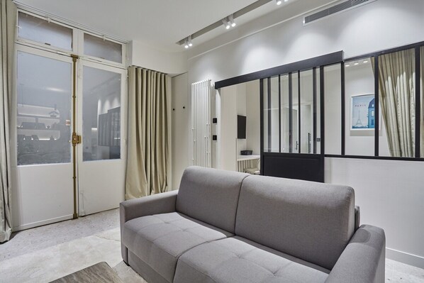 Una sala de estar moderna con un sofá gris, un ventanal con cortinas, un radiador y un cuadro enmarcado en la pared.