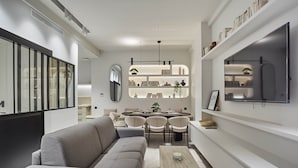 A modern living room with a grey sofa, a wooden coffee table, and a dining area with a round table and chairs.