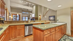 A spacious kitchen with wooden cabinets, a stainless steel dishwasher, granite countertops, and a large island. - Grandeur at Elevation 3 Bedroom Loft 3 Condo (Kirkwood)
