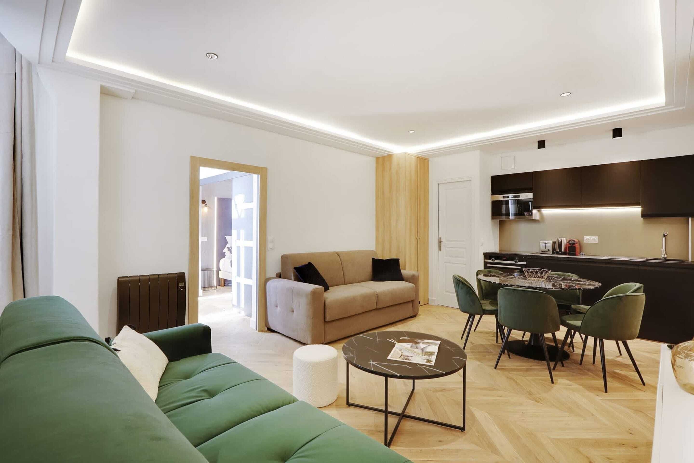 Een moderne woonkamer met een groene bank, een beige bank en een eethoek met een ronde tafel en stoelen.