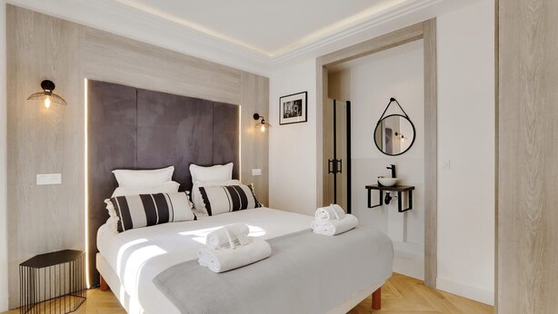 A modern hotel room with a large bed, bedside lamps, a small bedside table, and a mirror on the wall. - Sublime Apartment in the Heart of Paris (Paris)