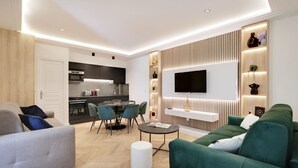 A modern living room with a green sofa, a white armchair, a dining area with a table and chairs, a kitchen in the background, and a flat-screen TV mounted on the wall. - Sublime Apartment in the Heart of Paris (Paris)