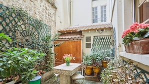 A courtyard with a stone table and chairs, surrounded by potted plants and a wooden door. - Superbe Apartment Le Marais/place des Vosges (Paris)
