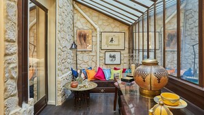 A cozy room with a stone wall, a wooden bench with colorful cushions, a glass table with a teapot, and a large decorative pot. - Superbe Apartment Le Marais/place des Vosges (Paris)