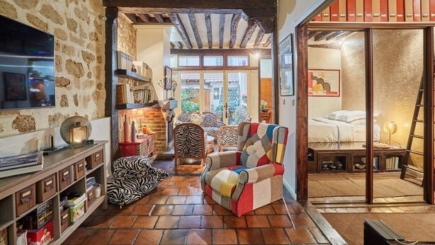 A cozy room with a stone wall, wooden beams, a colorful armchair, a zebra-patterned chair, and a bed with a ladder. - Superbe Apartment Le Marais/place des Vosges (Paris)