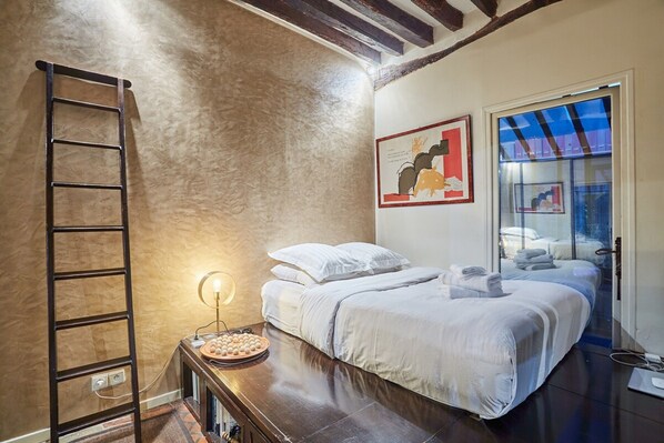 A bedroom with a wooden ladder, a bedside table with a lamp, a bed with white bedding, and a painting on the wall. - Superbe Apartment Le Marais/place des Vosges (Paris)