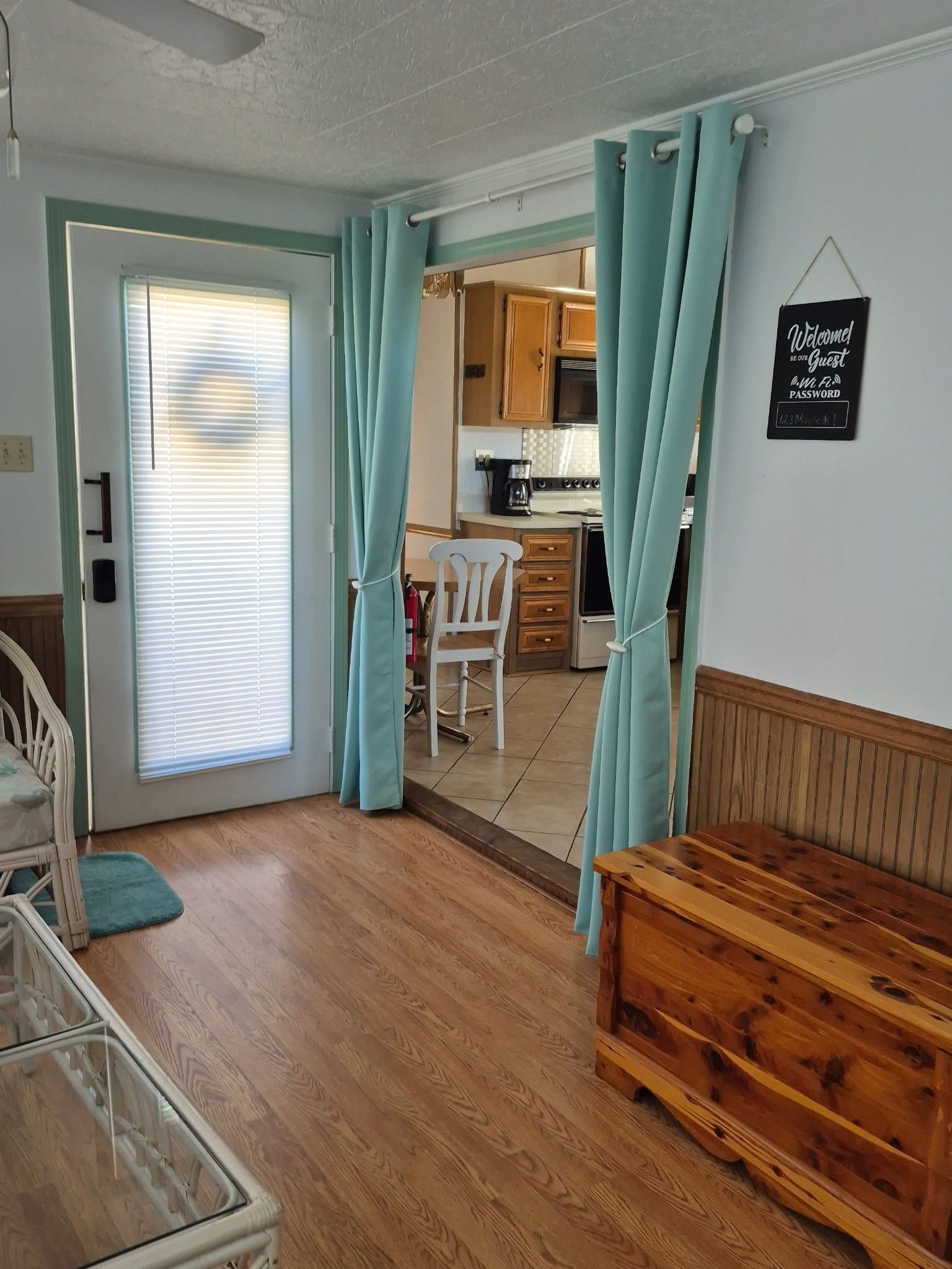 A room with a wooden bench, a white chair, a kitchen area with cabinets, and a sign on the wall.