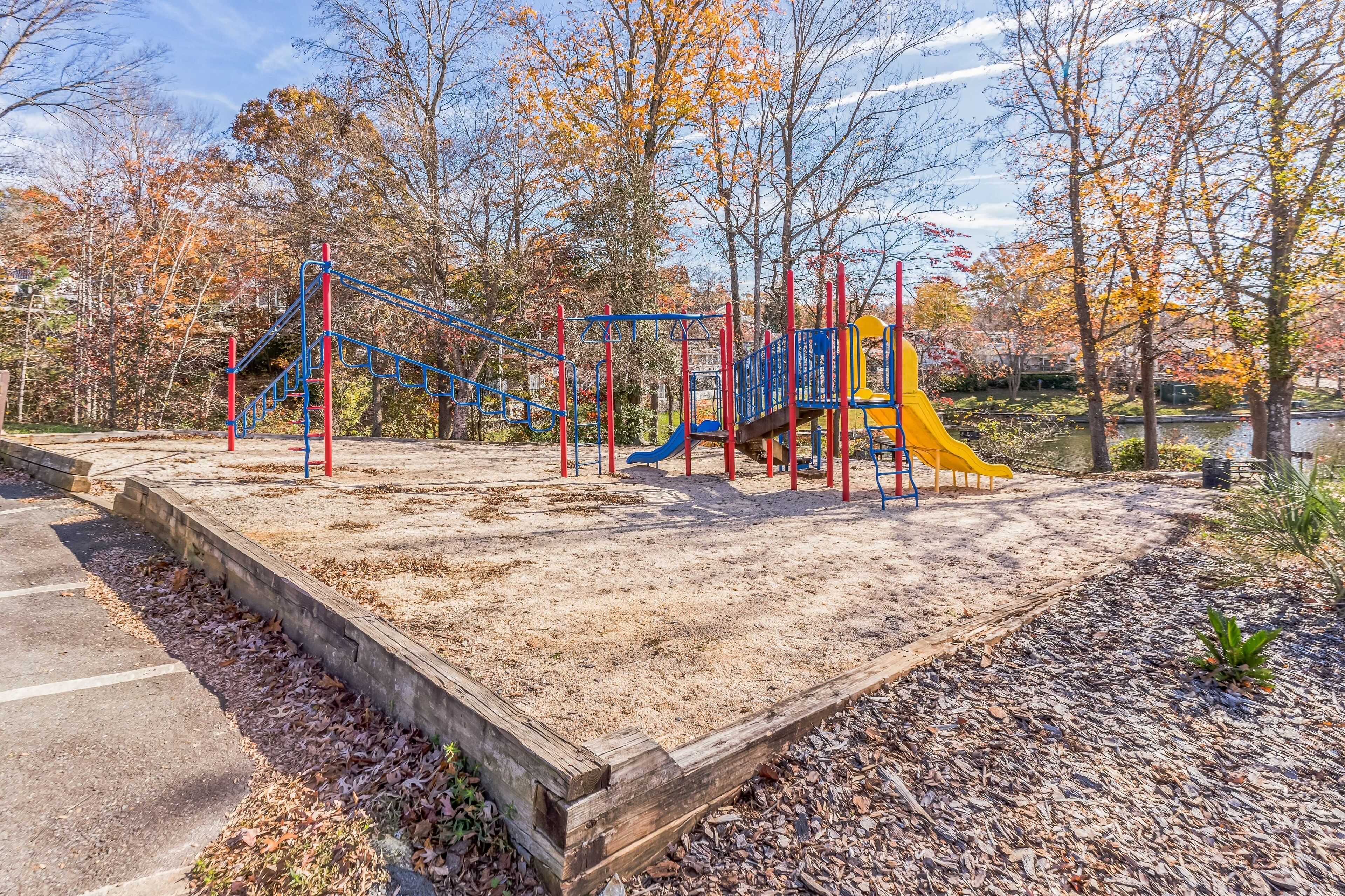 A playground with various play structures, surrounded by trees and a body of water.