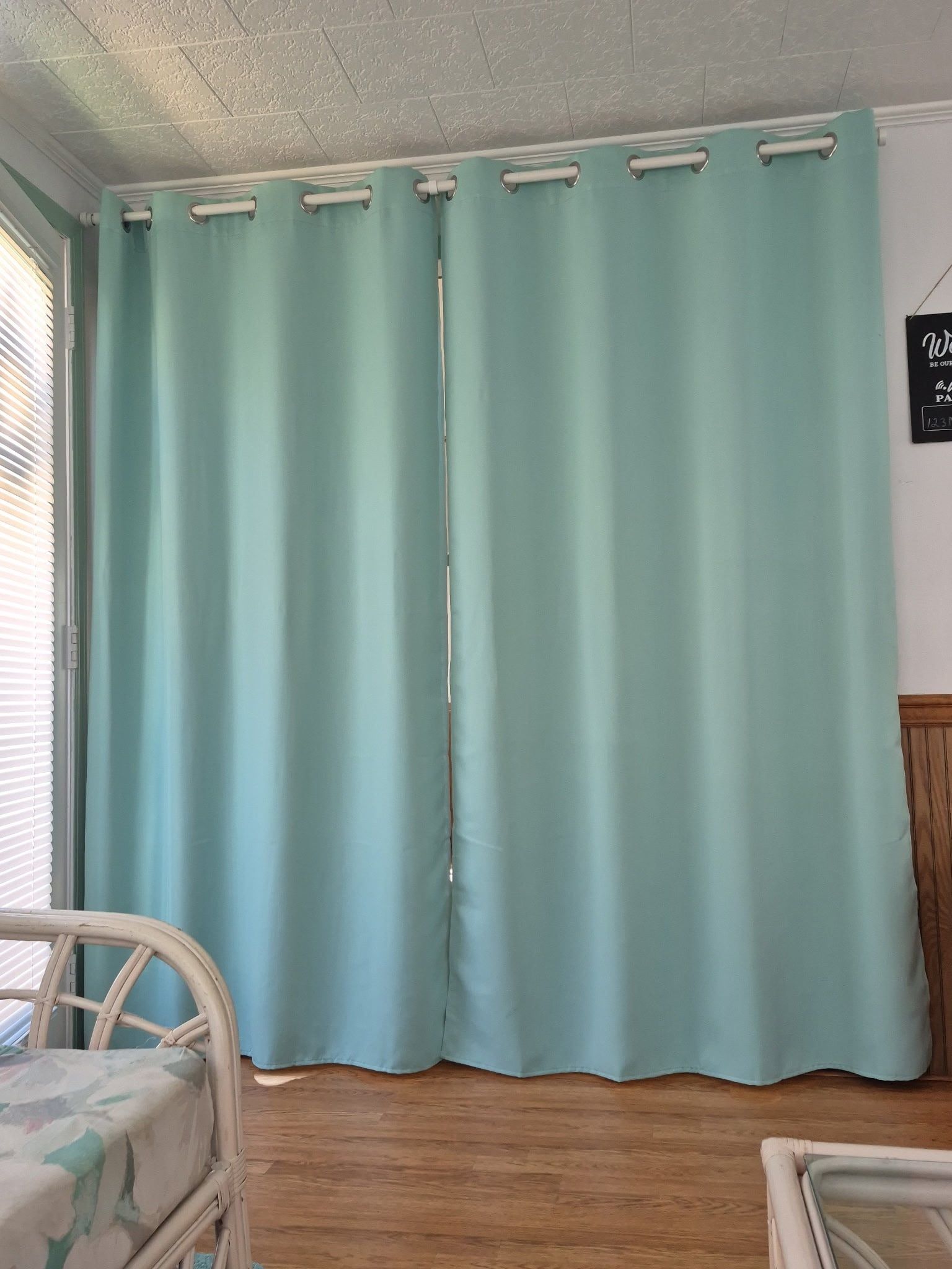 Una habitación con una cama, un ventanal con persianas y una pared con un cartel.