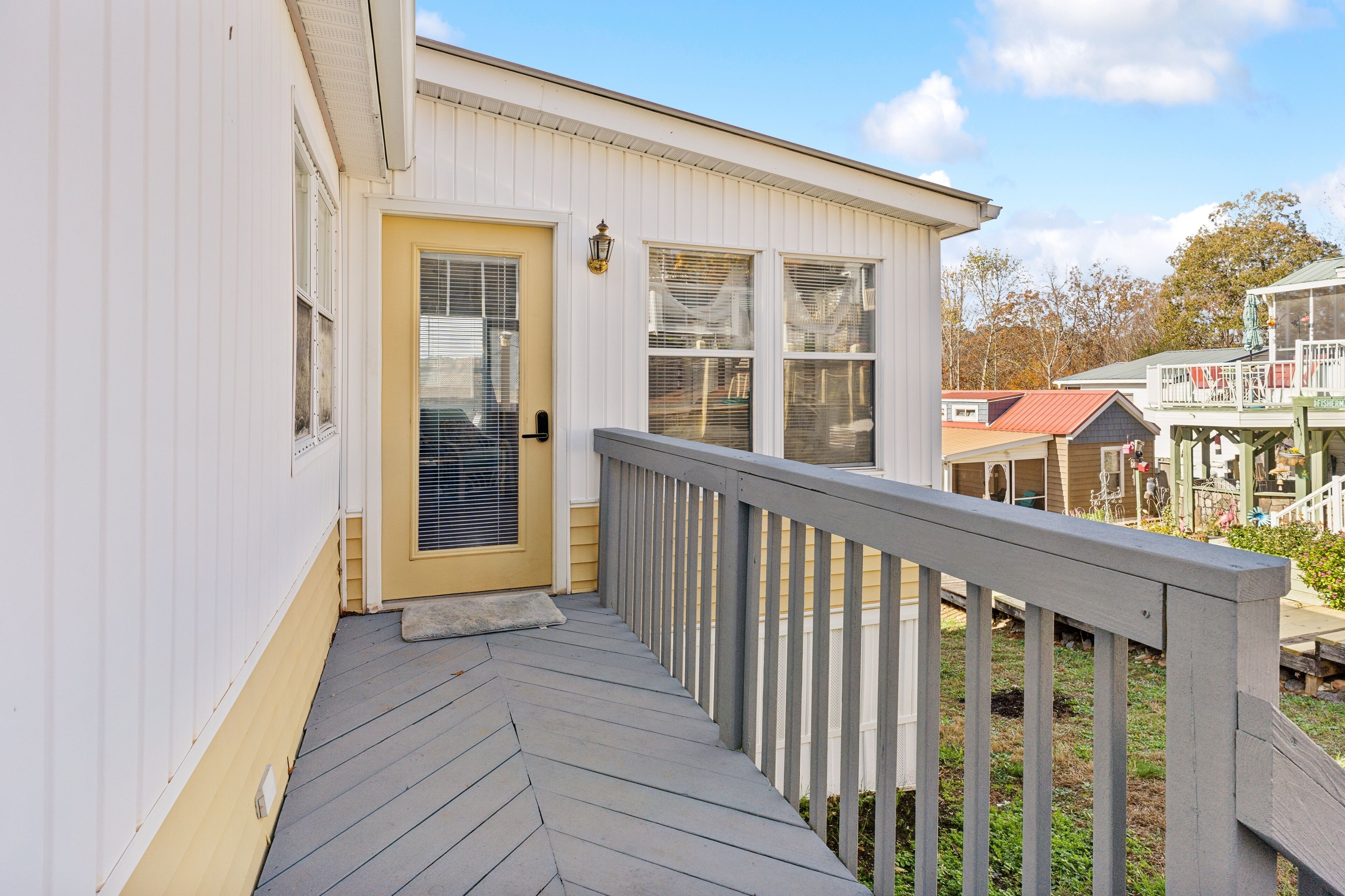 Un bâtiment blanc avec une porte jaune, une terrasse en bois et un petit porche doté d’une balustrade.