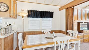 A dining area with a wooden table, white chairs, a clock, and a window with blinds.
