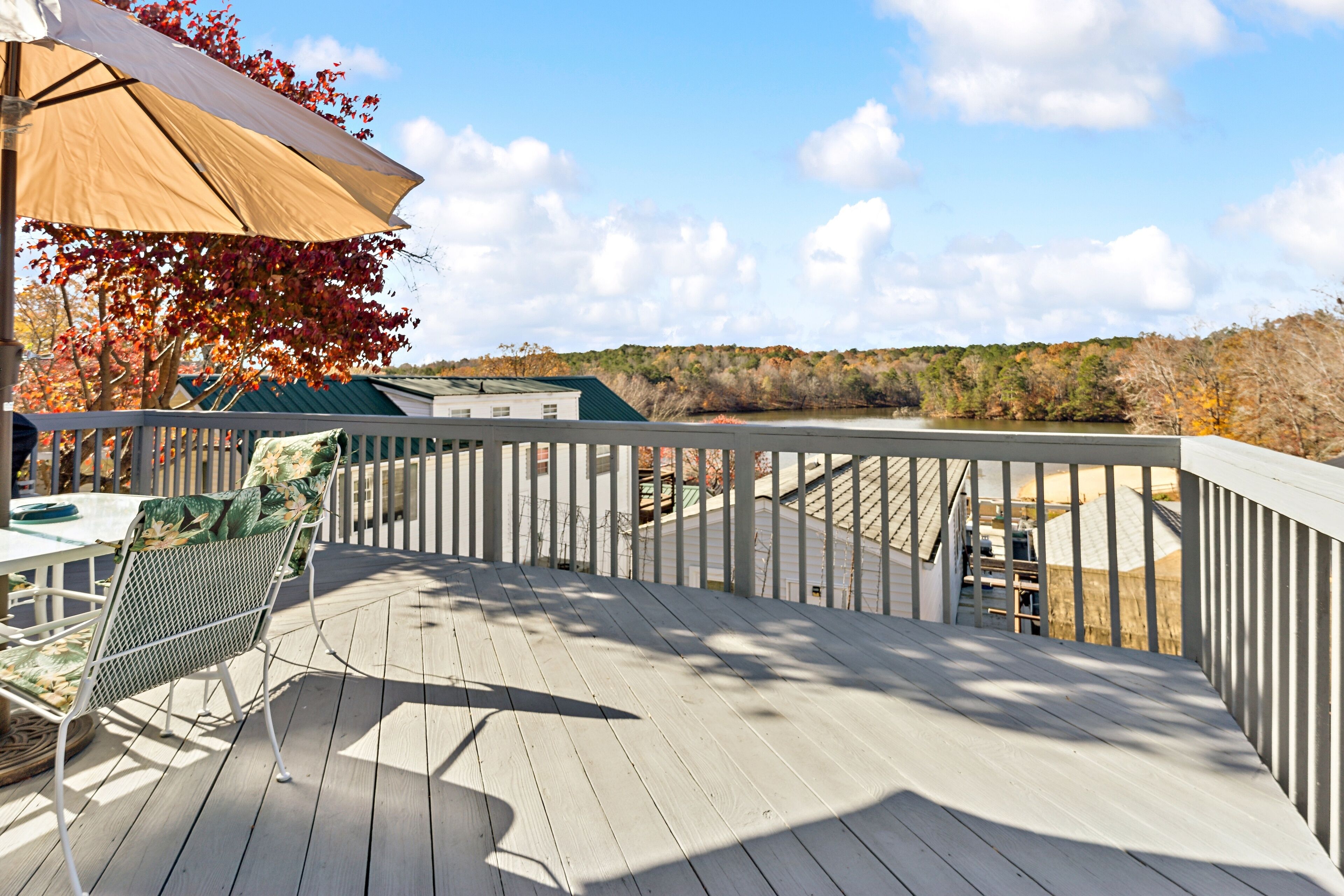A wooden deck with a white railing, a table with chairs, and a large umbrella.