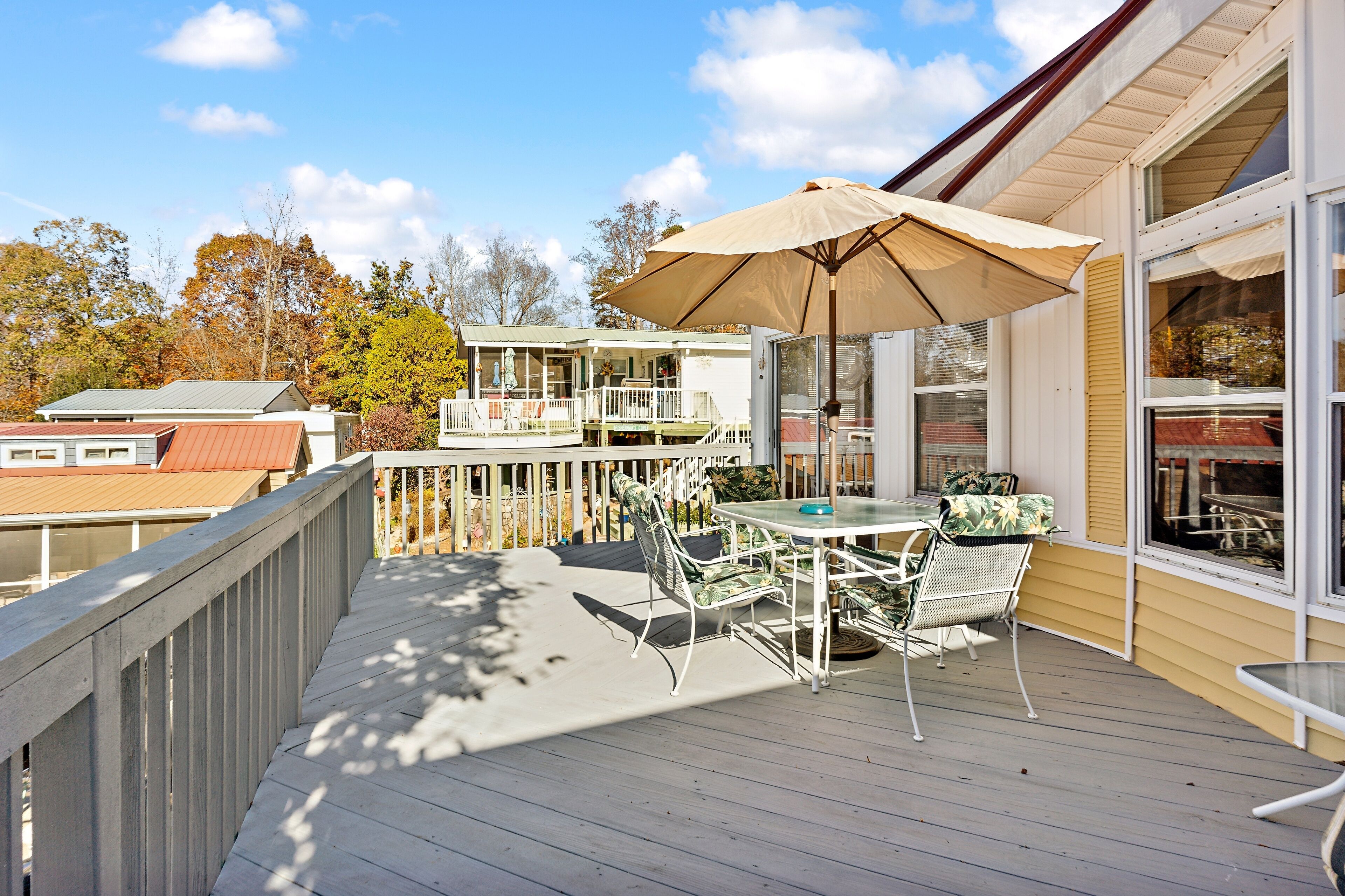 A wooden deck with a table and chairs, an umbrella, and a view of a building with a balcony.