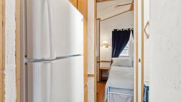 A narrow hallway leading to a bedroom with a bed, a nightstand, and a window with curtains.