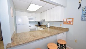 Eine Küche mit weißen Schränken, einer Granit-Arbeitsplatte, einem Kühlschrank, einem Herd und zwei Barhocker.