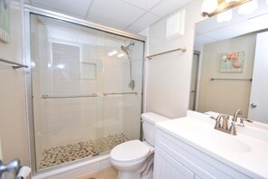 A modern bathroom with a glass-enclosed shower, a white toilet, and a vanity with a sink and mirror.