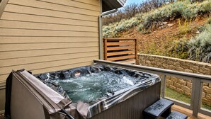 Un bain à remous sur une terrasse en bois, avec un mur en pierre et une vue sur un paysage aride et vallonné.