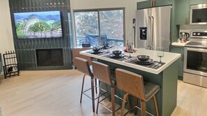 Une cuisine moderne dotée d’un grand îlot central, d’appareils électroménagers en acier inoxydable et d’un téléviseur fixé au mur.