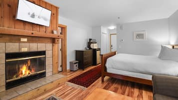 A bedroom with a fireplace, a bed, a dresser, and a television mounted on the wall.