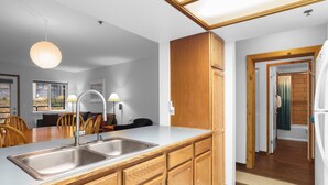 A modern kitchen with wooden cabinets, a stainless steel sink, and a dining area with chairs and a table. - Kirkwood Retreat - 2 Bedroom Condo 2 Condo (Kirkwood)