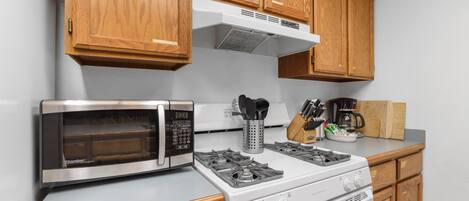 A kitchen with wooden cabinets, a microwave, a stove, and various kitchen utensils.