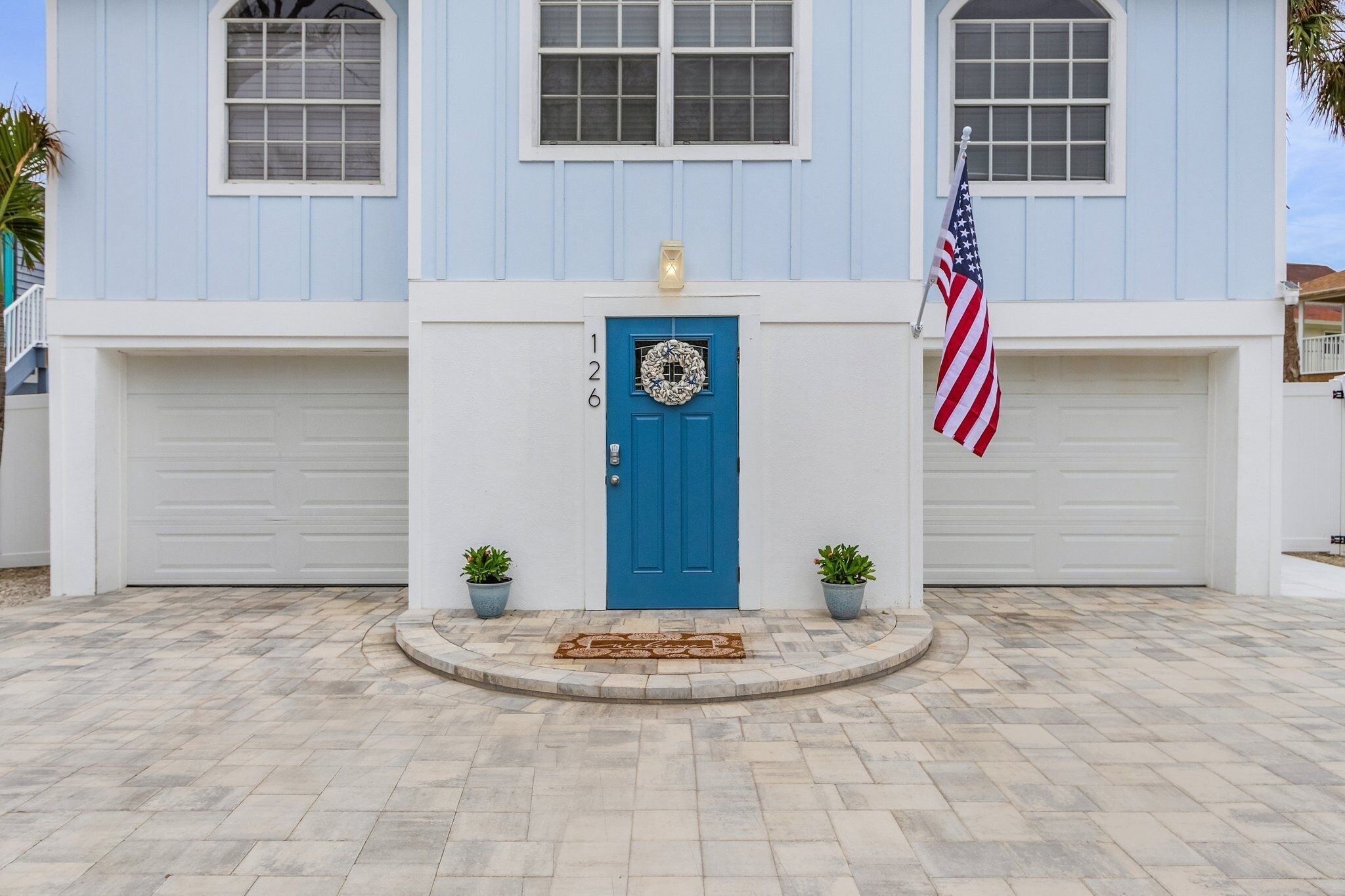 Une maison à deux étages avec une porte d’entrée bleue, une couronne décorative et un drapeau américain.