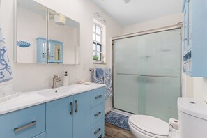 A bathroom with a white sink, blue cabinets, a glass shower enclosure, and a white toilet.