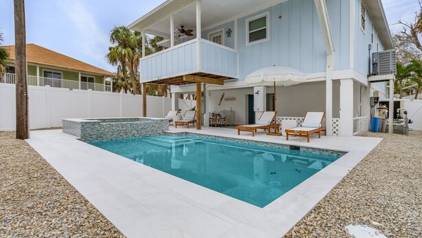 Ein zweistöckiges Haus mit Schwimmbad, Außenbereich mit Sitzgelegenheiten und einer überdachten Terrasse.