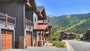 A row of modern, multi-story buildings with wooden balconies and large garage doors, set against a backdrop of a mountain range. - Luxury Home - Sleeps 10 - Fireplace & Mountain View 3 Bedroom Condo (Keystone)