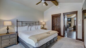 A bedroom with a large bed, two bedside tables with lamps, a ceiling fan, and a wooden door leading to another room. - Luxury Home - Sleeps 10 - Fireplace & Mountain View 3 Bedroom Condo (Keystone)