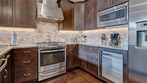 A modern kitchen with wooden cabinets, stainless steel appliances, a built-in oven, microwave, and dishwasher. - Luxury Home - Sleeps 10 - Fireplace & Mountain View 3 Bedroom Condo (Keystone)