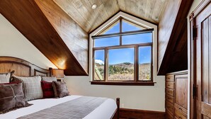 A bedroom with a large window, wooden ceiling beams, a bed with multiple pillows, and a wooden dresser. - Stunning Views - Renovated Condo In Pines Lodge 2 Bedroom Condo (Avon)