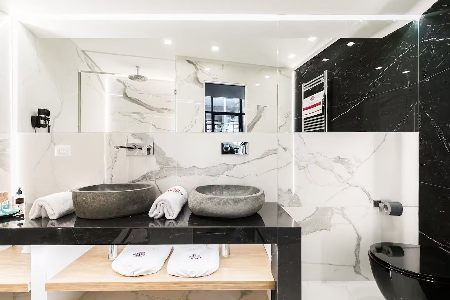 Une salle de bain moderne avec deux grands lavabos ronds en pierre, un miroir, un porte-serviettes et un meuble-lavabo en bois.