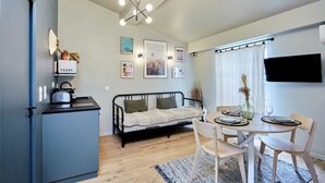 A compact living space with a kitchenette, a sofa, a dining table with chairs, and a mounted TV.
