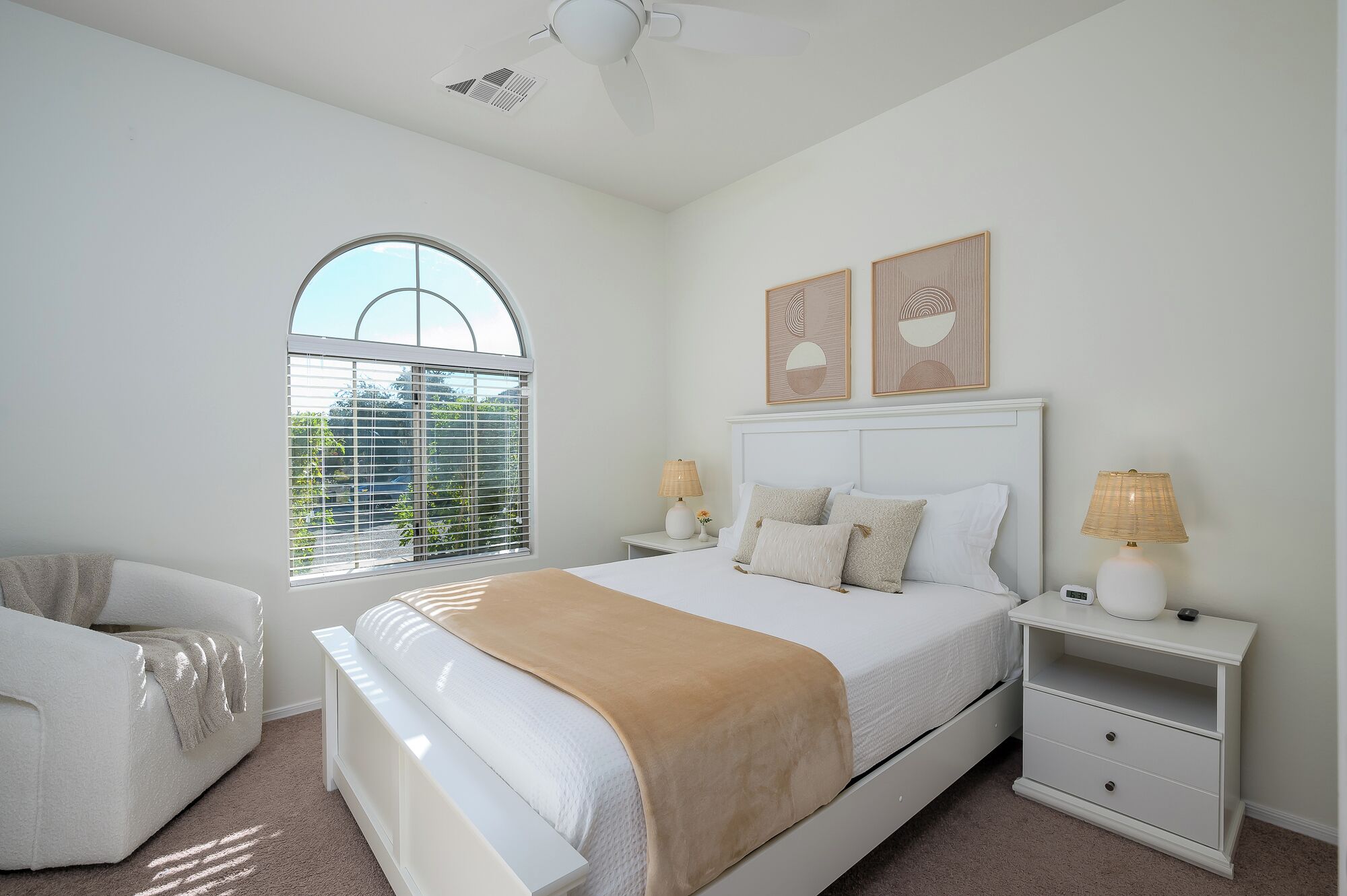 A bedroom with a large bed, two bedside tables with lamps, a window with blinds, and a ceiling fan.