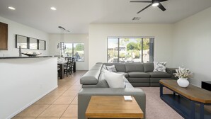 Uma sala de estar moderna com um sofá cinza, uma mesa de centro de madeira e uma área de jantar com um jogo de mesa preto e branco.