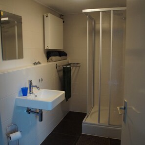 Un baño con un lavabo blanco, un espejo, toallero y cabina de ducha de vidrio.