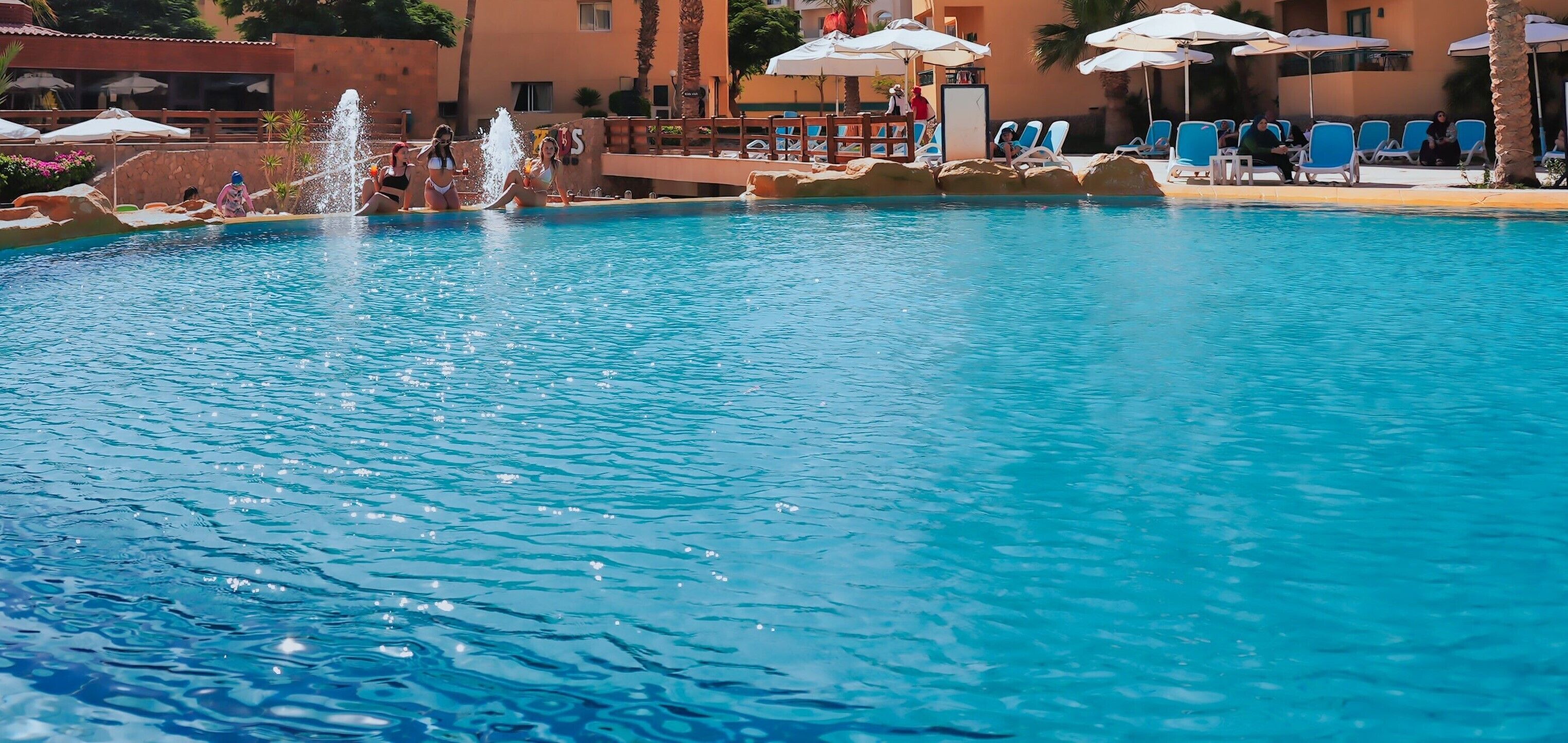 Una piscina con fuente de agua, rodeada de sillones de playa y sombrillas.